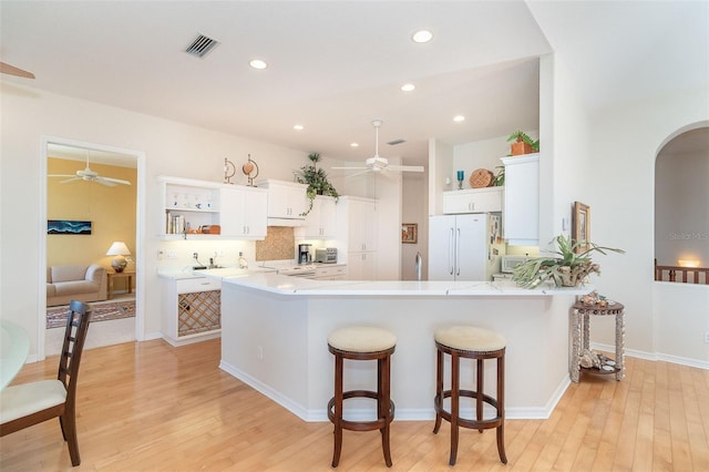 kitchen featuring white cabinetry, a breakfast bar area, kitchen peninsula, white appliances, and light hardwood / wood-style flooring