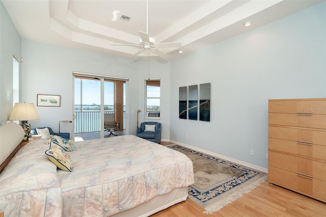 bedroom featuring access to exterior, a tray ceiling, ceiling fan, and light wood-type flooring