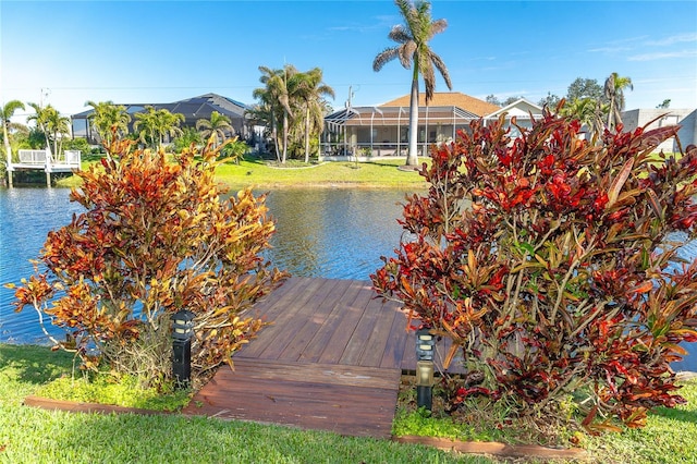 view of dock with a water view, glass enclosure, and a lawn