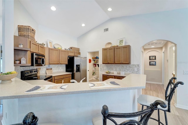 kitchen featuring stainless steel appliances, a kitchen breakfast bar, kitchen peninsula, and vaulted ceiling