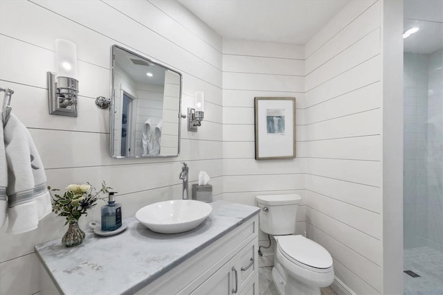 bathroom with vanity, toilet, wooden walls, and a tile shower