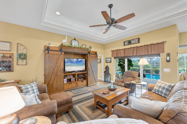 living room with ceiling fan, a barn door, and a raised ceiling