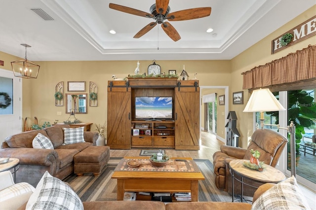 living room with hardwood / wood-style floors, ceiling fan with notable chandelier, a barn door, and a raised ceiling