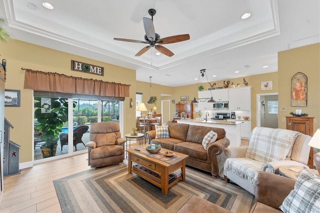 living room featuring sink, a tray ceiling, light hardwood / wood-style floors, and ceiling fan