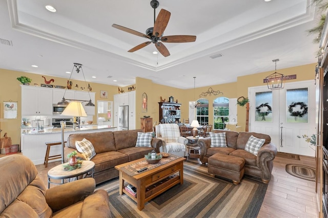 living room featuring hardwood / wood-style flooring, ceiling fan, a raised ceiling, and french doors