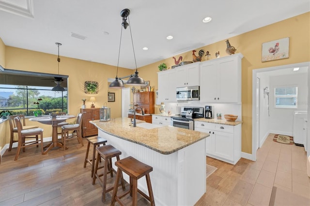 kitchen featuring sink, appliances with stainless steel finishes, white cabinets, a center island with sink, and decorative light fixtures