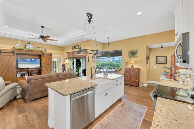 kitchen with appliances with stainless steel finishes, pendant lighting, a barn door, light stone countertops, and white cabinets