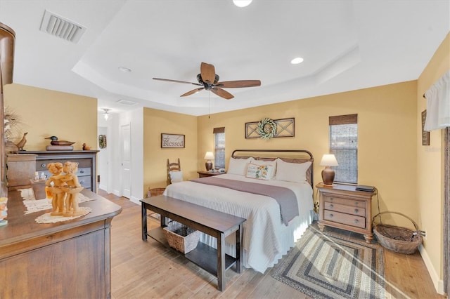 bedroom featuring ceiling fan, a tray ceiling, and light hardwood / wood-style floors