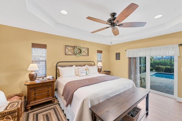 bedroom featuring multiple windows, access to exterior, ceiling fan, and a tray ceiling