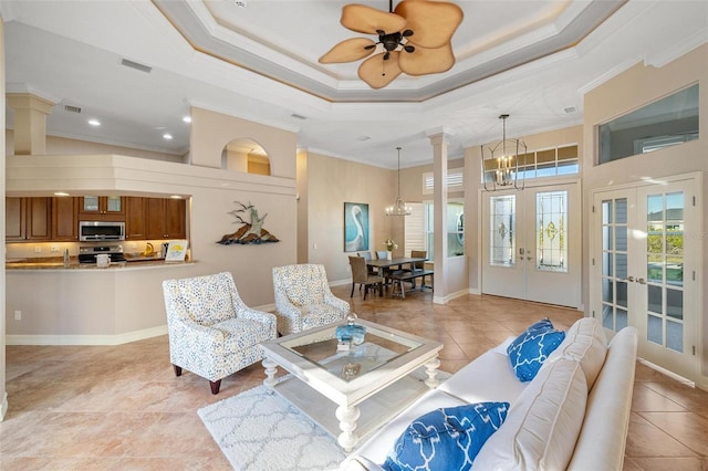 tiled living room featuring a tray ceiling, crown molding, french doors, and a chandelier