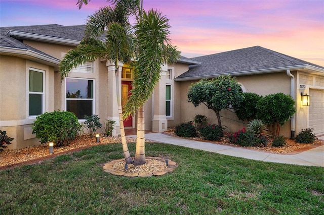 view of front of house featuring stucco siding, a front yard, an attached garage, and a shingled roof