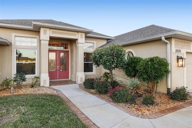 view of exterior entry with stucco siding, french doors, a garage, and a shingled roof