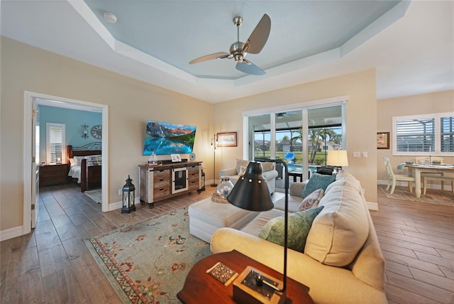 living room featuring ceiling fan, plenty of natural light, dark hardwood / wood-style floors, and a raised ceiling