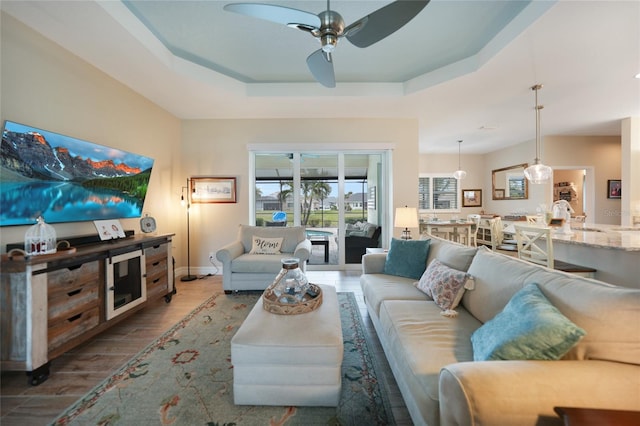 living room featuring ceiling fan, a tray ceiling, and dark hardwood / wood-style flooring