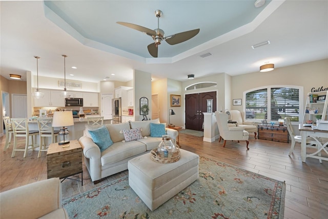 living room featuring a tray ceiling, ceiling fan, and light wood-type flooring