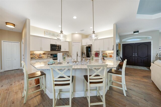 kitchen featuring hanging light fixtures, white cabinetry, appliances with stainless steel finishes, and a kitchen island with sink