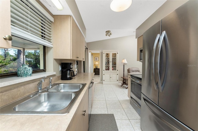 kitchen featuring lofted ceiling, sink, light tile patterned floors, stainless steel appliances, and light brown cabinetry