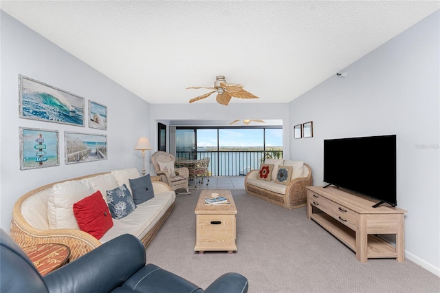 living area featuring carpet floors, vaulted ceiling, ceiling fan, a textured ceiling, and baseboards