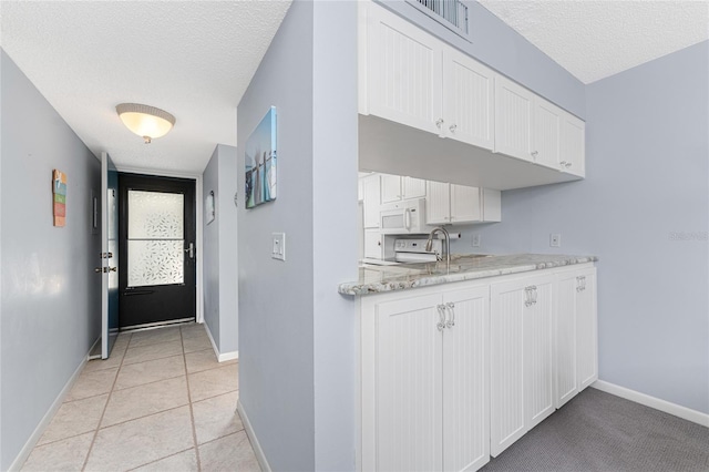 kitchen with white appliances, white cabinetry, a textured ceiling, and baseboards