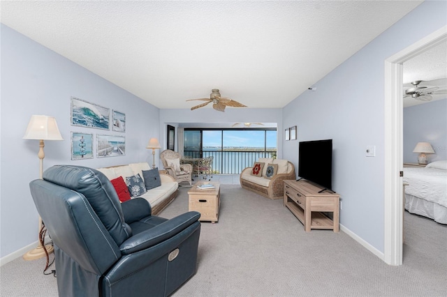 living area featuring carpet floors, a textured ceiling, baseboards, and a ceiling fan