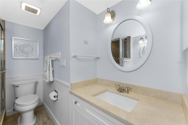 bathroom featuring visible vents, toilet, a wainscoted wall, a shower with door, and vanity