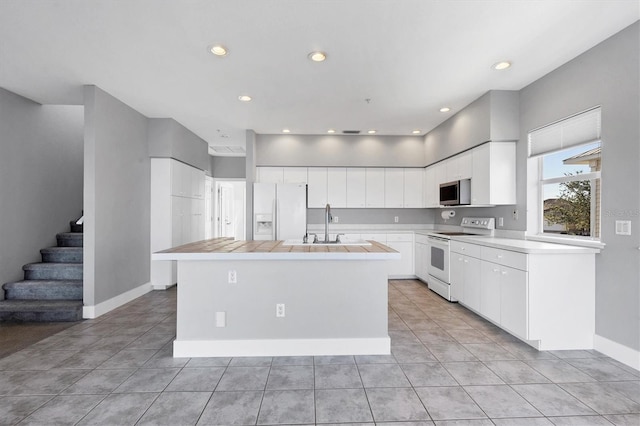 kitchen with white appliances, light tile patterned floors, a kitchen island, and white cabinets