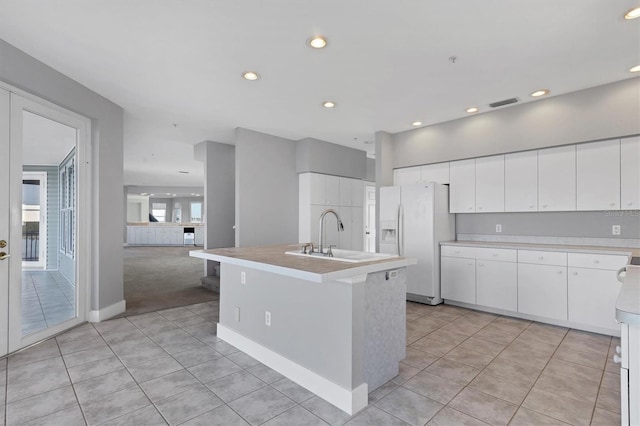 kitchen with sink, white cabinetry, white refrigerator with ice dispenser, an island with sink, and light tile patterned flooring