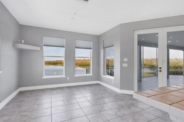 tiled empty room with plenty of natural light, french doors, and a water view