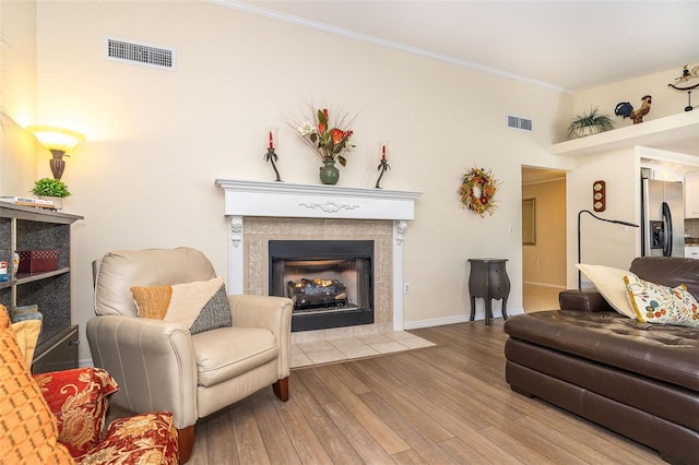 living area with a tile fireplace, visible vents, wood finished floors, and ornamental molding