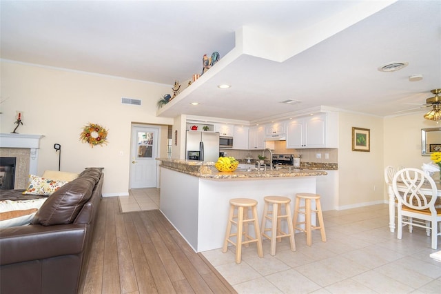 kitchen featuring light stone counters, a tile fireplace, open floor plan, appliances with stainless steel finishes, and ornamental molding