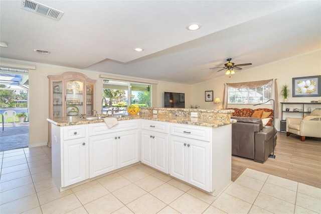 kitchen with a sink, visible vents, open floor plan, vaulted ceiling, and light stone countertops