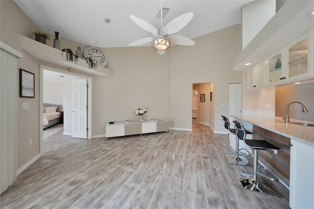 dining area featuring ceiling fan, light hardwood / wood-style floors, sink, and a high ceiling