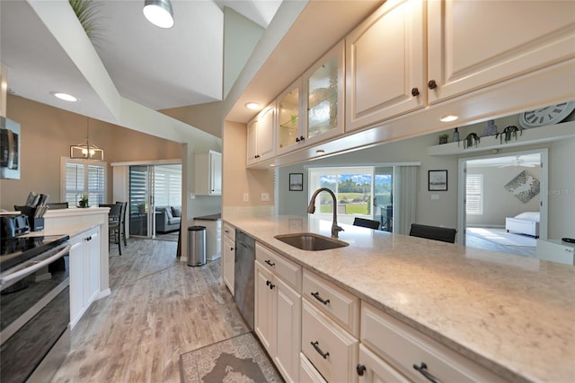 kitchen with sink, hanging light fixtures, stainless steel appliances, light stone countertops, and light wood-type flooring