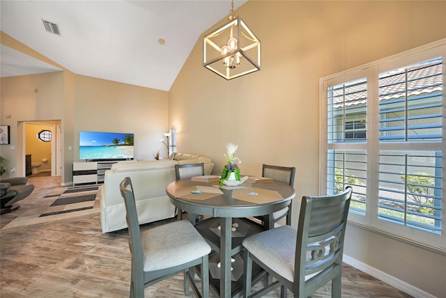 dining space with an inviting chandelier, high vaulted ceiling, and light hardwood / wood-style flooring