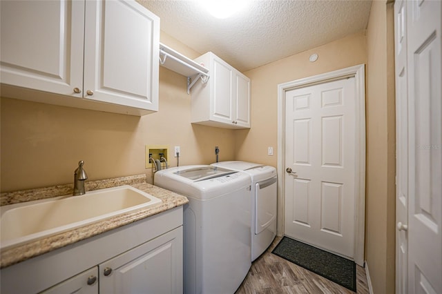 laundry area with wood-type flooring, sink, cabinets, independent washer and dryer, and a textured ceiling