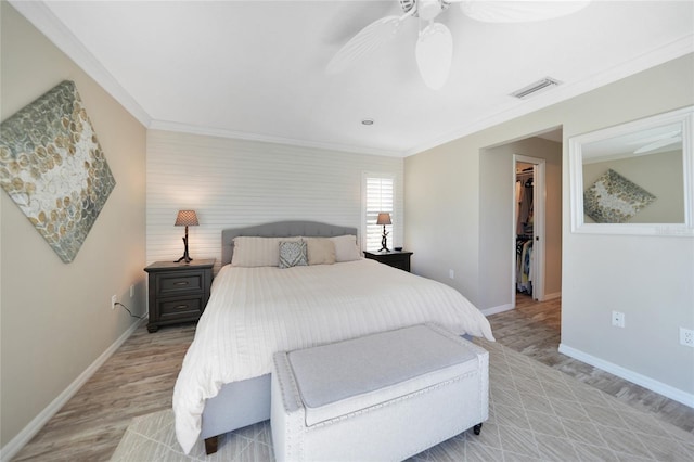 bedroom featuring crown molding, a walk in closet, ceiling fan, and light hardwood / wood-style floors