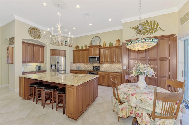 kitchen featuring appliances with stainless steel finishes, hanging light fixtures, light stone counters, tasteful backsplash, and an island with sink