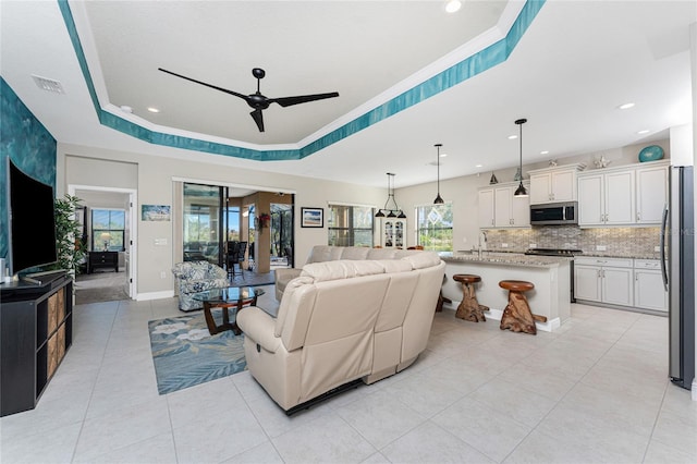 tiled living room with crown molding, ceiling fan, a raised ceiling, and sink