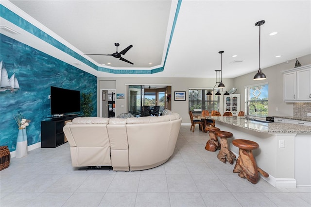 living room featuring a raised ceiling, sink, light tile patterned floors, and ceiling fan