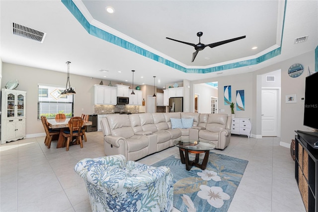 living room featuring a raised ceiling, ceiling fan, and light tile patterned flooring