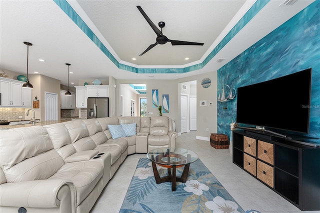 living room featuring light tile patterned floors, sink, a raised ceiling, and ceiling fan