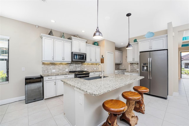 kitchen with pendant lighting, sink, appliances with stainless steel finishes, a kitchen island with sink, and white cabinetry