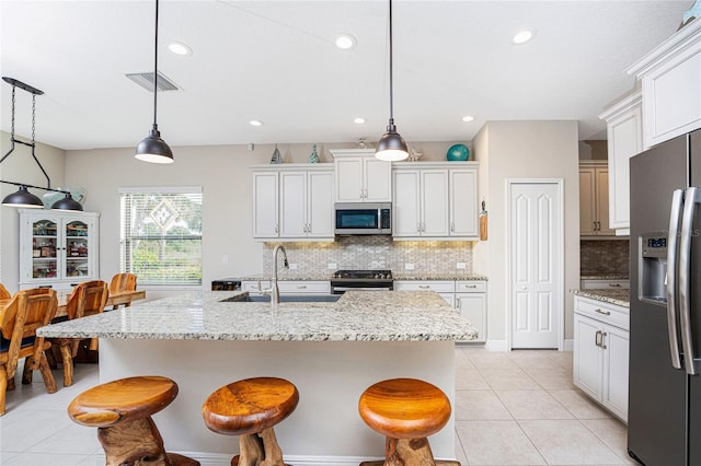 kitchen featuring sink, hanging light fixtures, light tile patterned floors, appliances with stainless steel finishes, and an island with sink