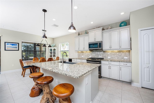 kitchen featuring appliances with stainless steel finishes, decorative light fixtures, sink, a kitchen island with sink, and light stone countertops