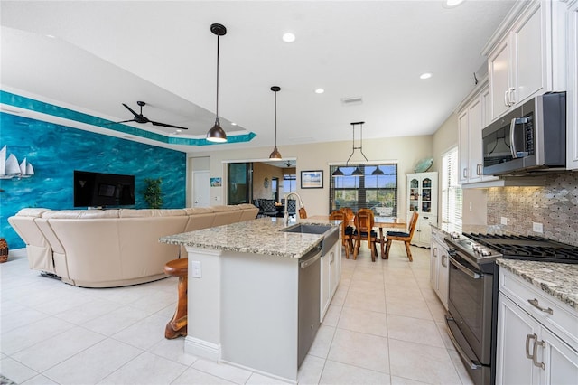 kitchen featuring white cabinetry, sink, hanging light fixtures, stainless steel appliances, and a center island with sink