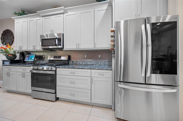 kitchen with light tile patterned floors, appliances with stainless steel finishes, white cabinets, dark stone counters, and backsplash