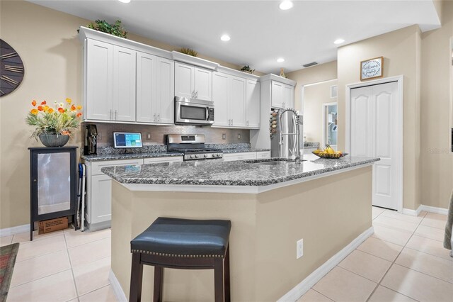 kitchen with white cabinetry, light tile patterned flooring, appliances with stainless steel finishes, and a kitchen island with sink