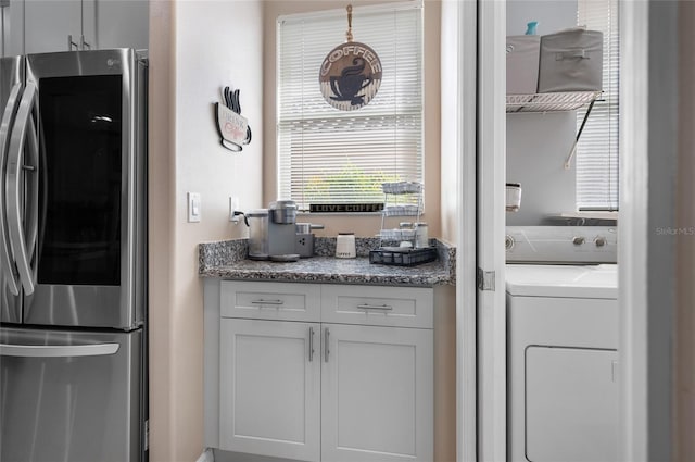 kitchen featuring stainless steel refrigerator, washer / clothes dryer, light stone countertops, and white cabinets