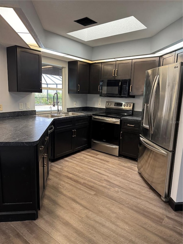 kitchen featuring a skylight, appliances with stainless steel finishes, sink, and light hardwood / wood-style flooring