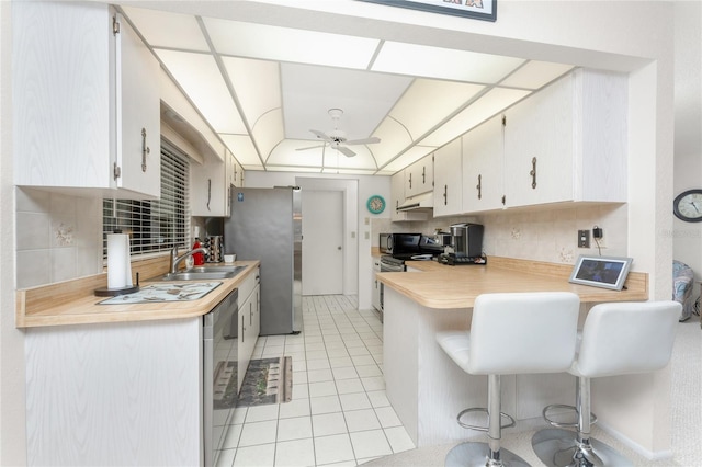 kitchen with sink, a breakfast bar area, appliances with stainless steel finishes, ceiling fan, and decorative backsplash